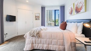 A hotel room with a bed, a TV mounted on the wall, a window with curtains, and artwork on the wall. - Large Stylish 1BR Apartment + Carpark in CBD (Auckland Central)