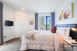 A hotel room with a bed, a TV mounted on the wall, a window with curtains, and artwork on the wall. - Large Stylish 1BR Apartment + Carpark in CBD (Auckland Central)