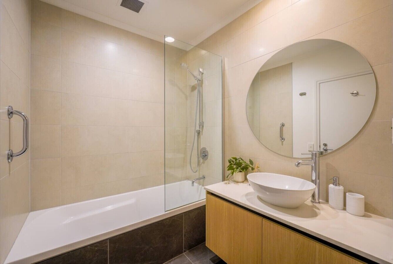 A modern bathroom with a glass-enclosed shower, a freestanding bathtub, and a round mirror above a sink with a vessel basin.