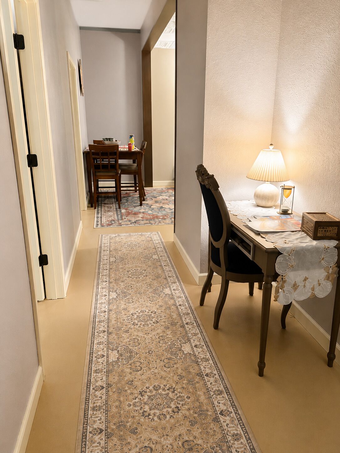 A hallway with a dining area, a rug, a table with a lamp, and a chair.