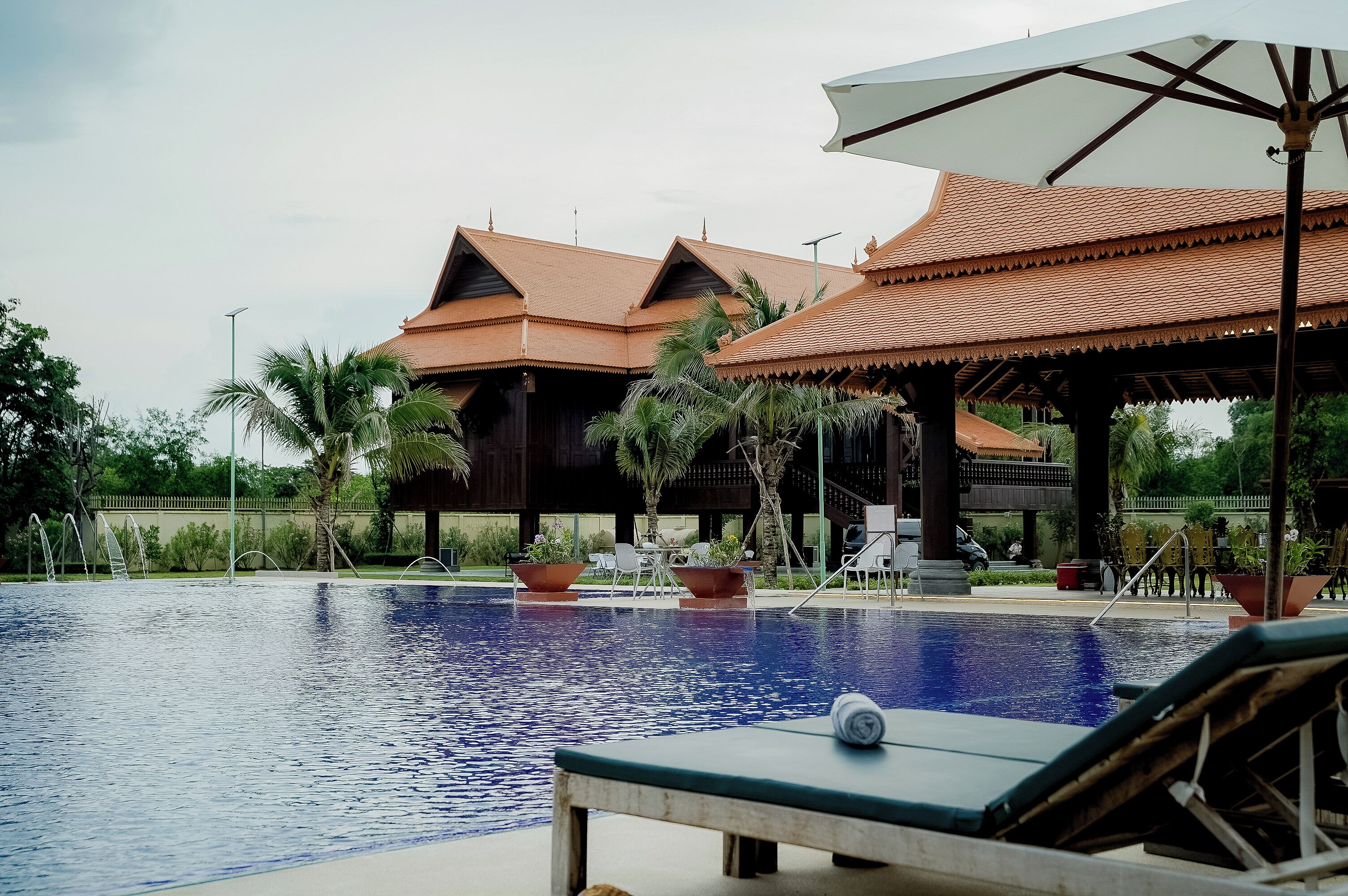 A swimming pool with lounge chairs and umbrellas, surrounded by traditional buildings with tiled roofs.