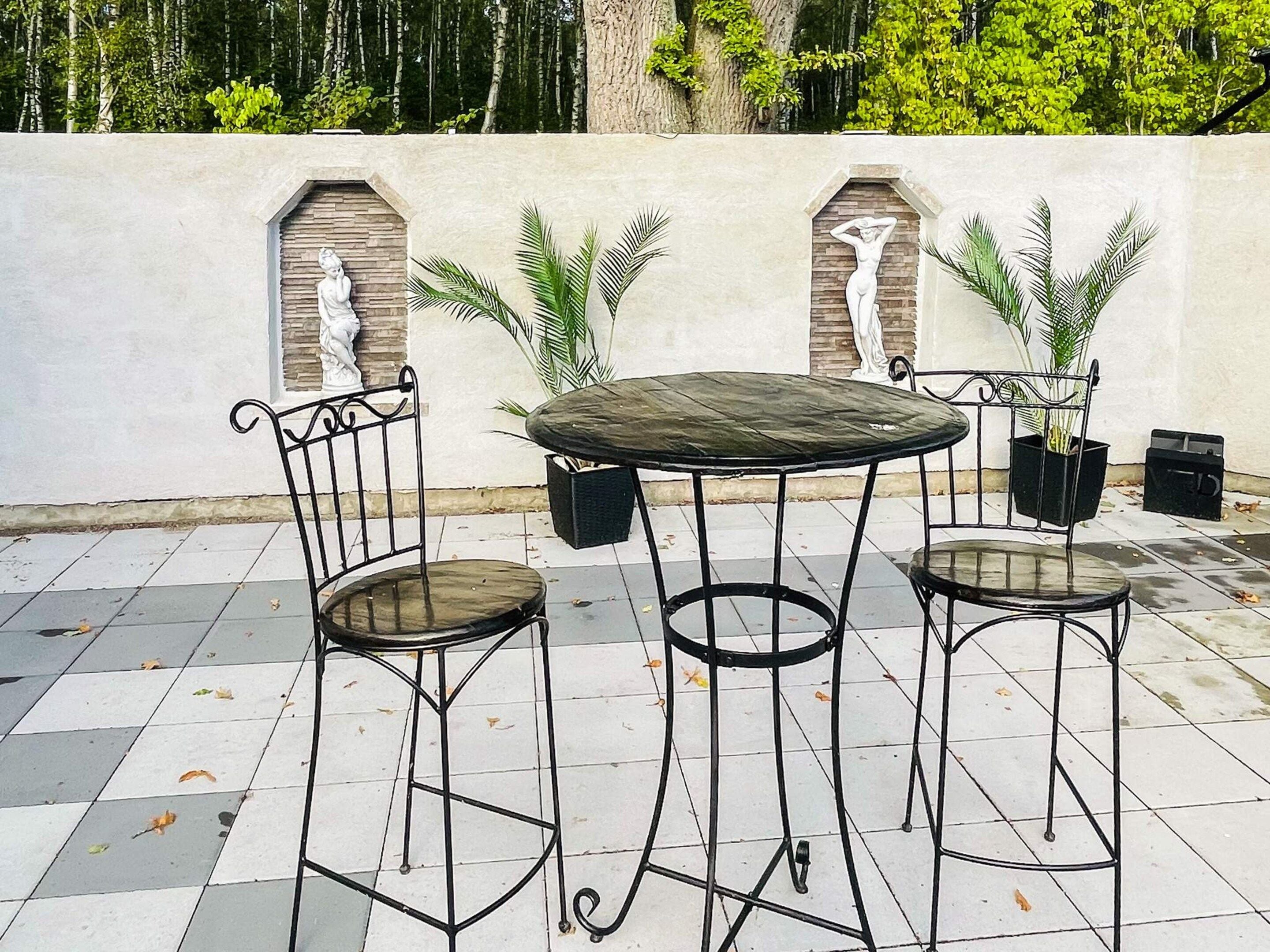 A patio with a round table and two chairs, surrounded by potted plants and decorative wall niches.