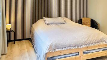 A single-bed room with a wooden frame, a ruffled bed skirt, and a bedside table with a lamp.