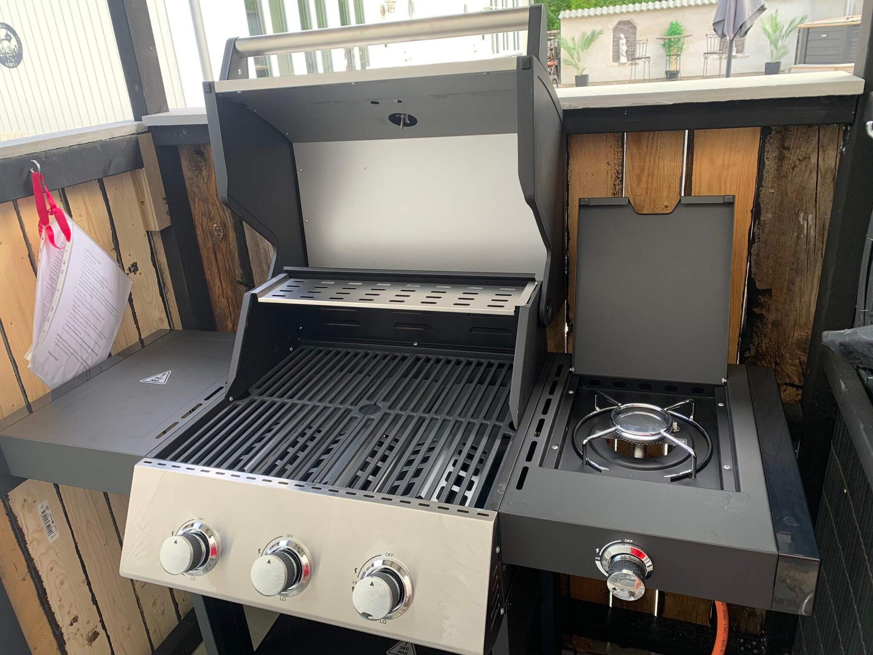 Una parrilla portátil con panel de control, quemador a gas y tapa ventilada.