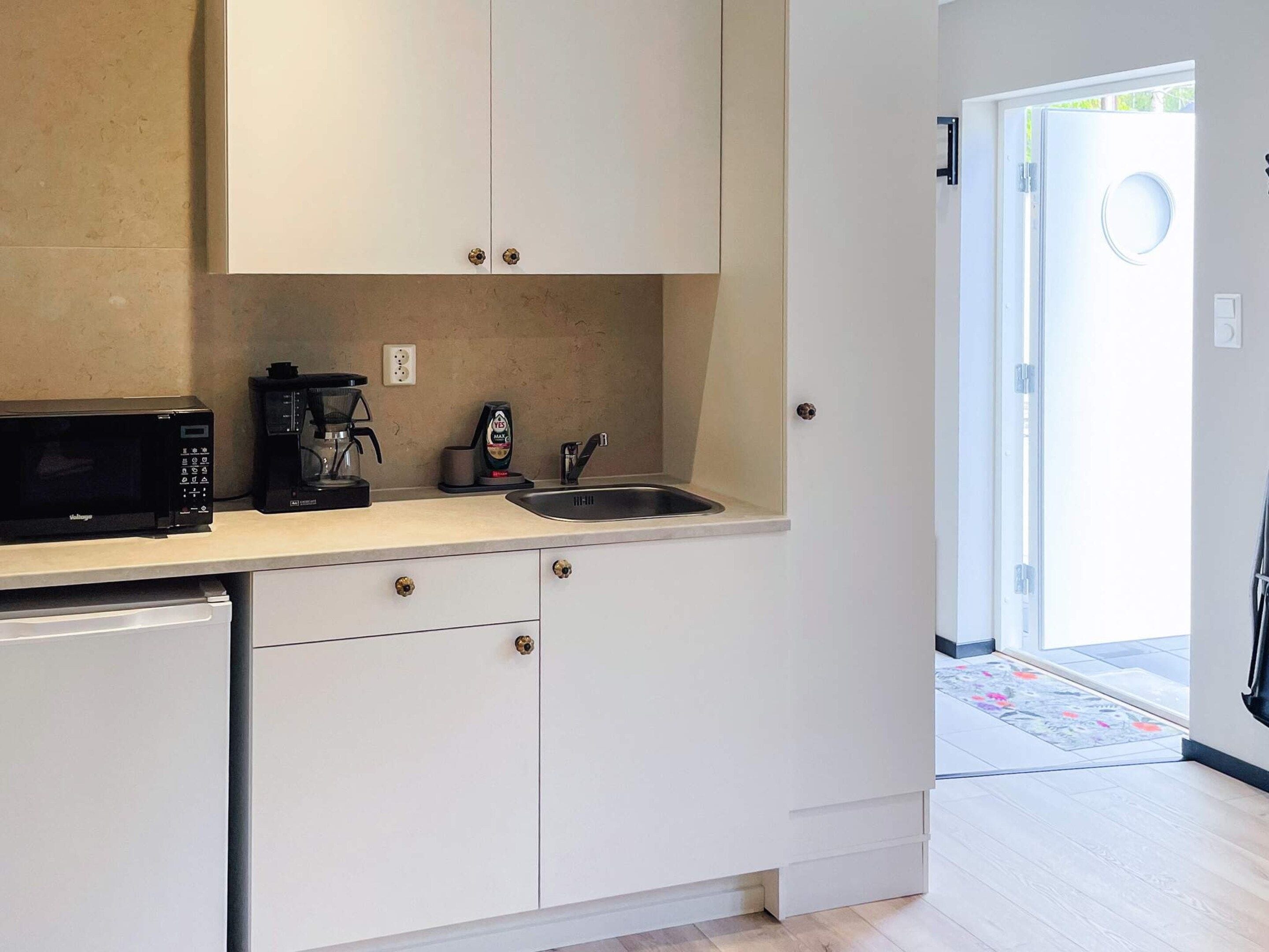 A compact kitchen with white cabinets, a black microwave, a coffee maker, and a sink.