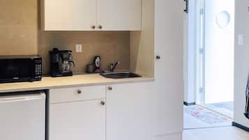 A compact kitchen with white cabinets, a black microwave, a coffee maker, and a sink.