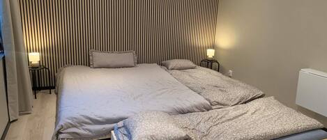 Una cama doble con estructura de madera, dos mesitas de noche con lámparas, un aire acondicionado de pared y un diseño de rayas en la pared.