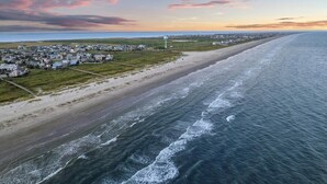 Vue aérienne d’une ville côtière avec une plage, des maisons et un phare.