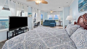 Une chambre avec un grand lit, une télévision, un ventilateur de plafond et une vue sur l’océan.