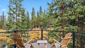 Une terrasse en bois avec deux fauteuils à bascule et une petite table, donnant sur une zone boisée avec un étang.