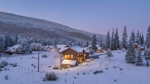 Ein mit Schnee bedecktes Chalet mit mehreren Holzhütten, umgeben von schneebedeckten Bäumen und einem Bergpanorama.