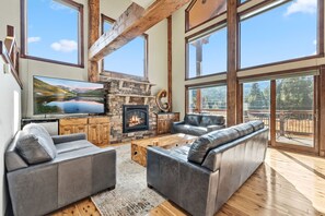 A spacious living room with a stone fireplace, large windows, and a cozy seating area. - Whispering Pines Retreat Hot Tub & Game Room (Breckenridge)