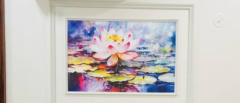 A hotel room with a bed, a framed painting of a lotus flower, and an air conditioning unit mounted on the wall.
