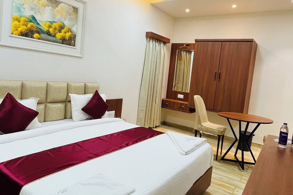 Une chambre d’hôtel avec un grand lit, un bureau, une chaise, une armoire et un ventilateur de plafond.