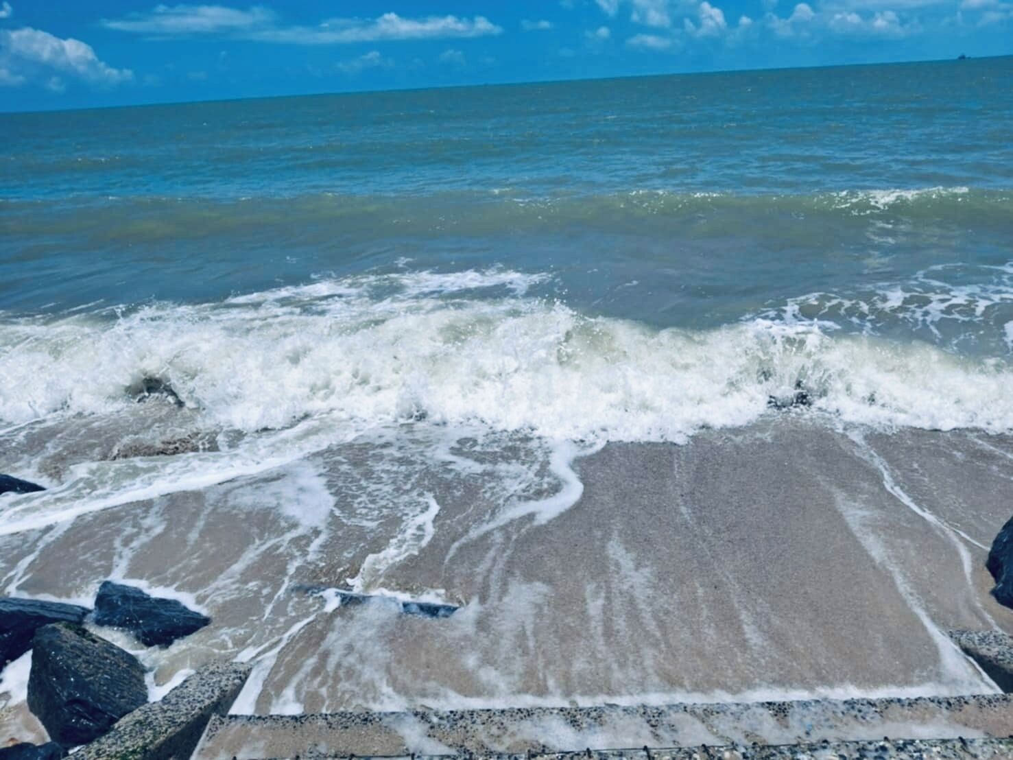 Ein Strand mit brechenden Wellen, einem klaren Himmel und weiter Fernsicht.