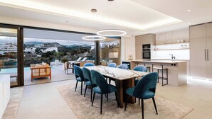 Une cuisine moderne dotée d’un grand îlot central, d’un coin repas avec une table en marbre et offrant une vue sur le paysage urbain.