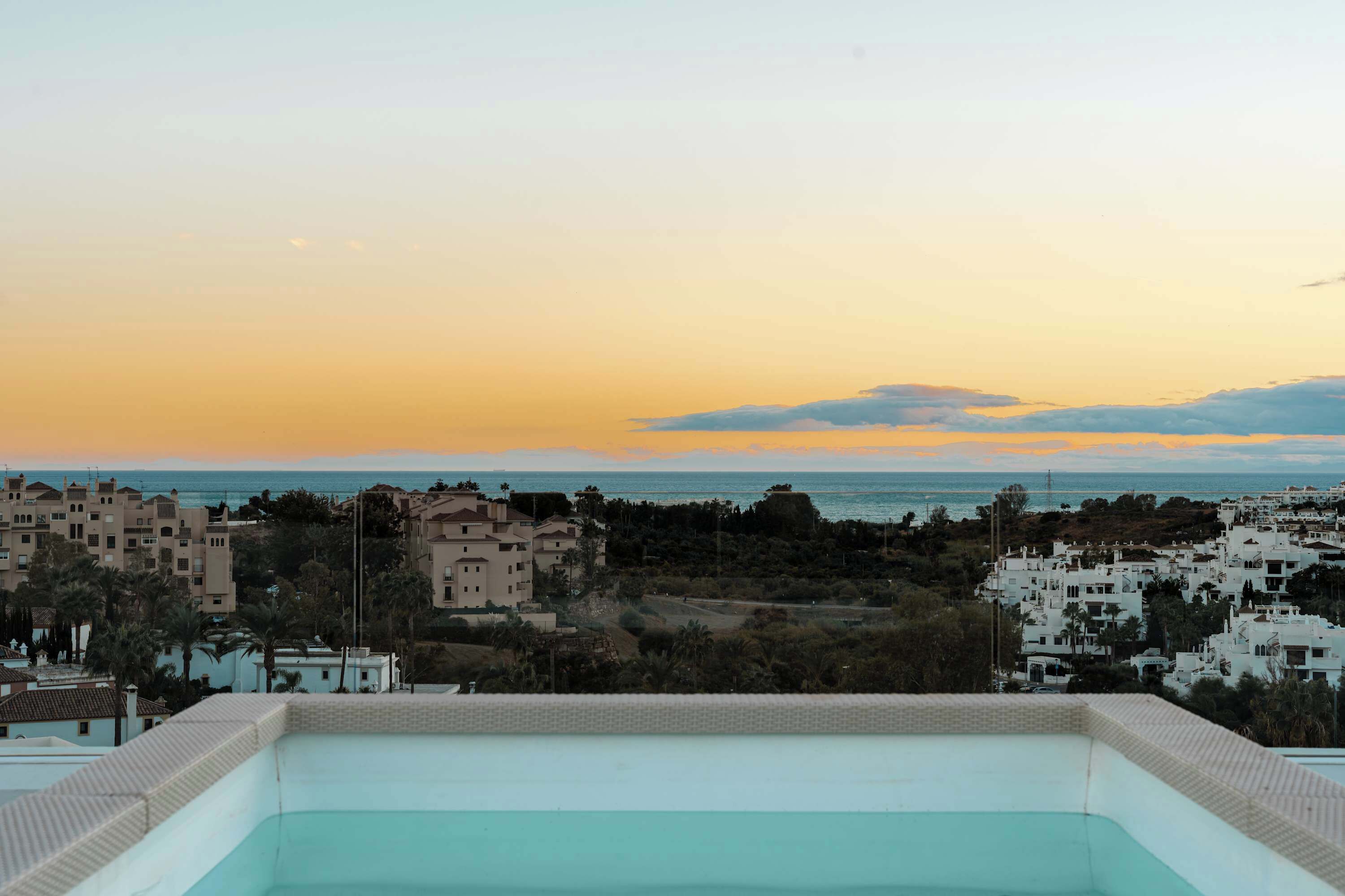 Piscina no terraço com vista para uma cidade costeira ao pôr do sol.