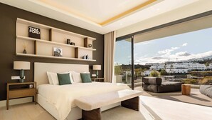 Une chambre moderne avec un grand lit, des tables de chevet, un banc et une vue sur le paysage urbain grâce à de grandes fenêtres.