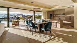 Une cuisine moderne dotée d’un grand îlot central, d’un coin repas avec une table et des chaises, et offrant une vue sur le paysage urbain grâce à de grandes fenêtres.