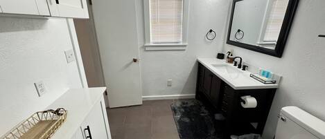 A bathroom with a white toilet, a sink with a mirror above it, and a door leading to another room.