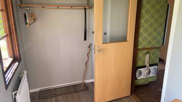 A room with a wooden door, a radiator, a window, and a shelf with folded items.