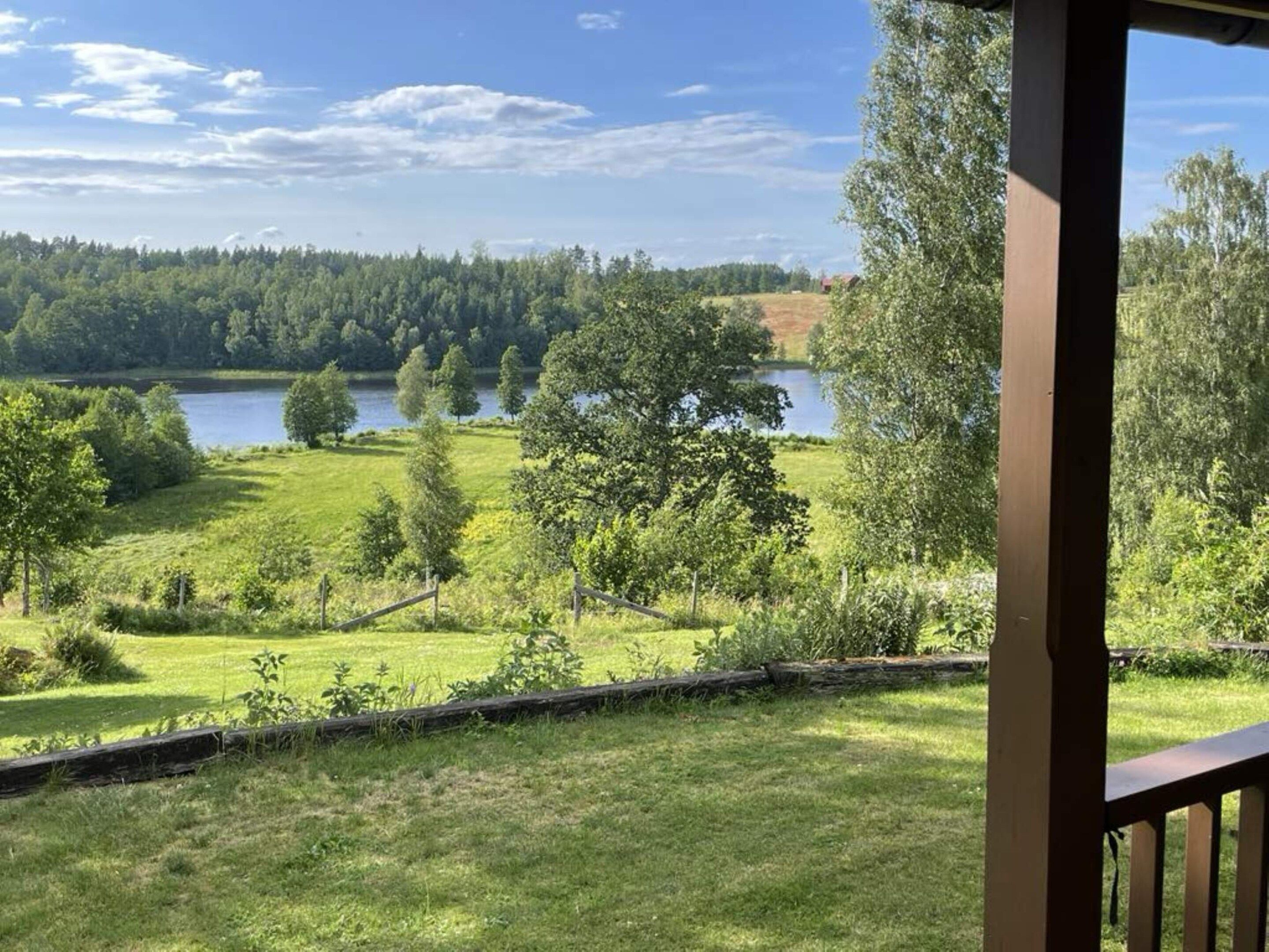 A view from a covered porch overlooking a lake surrounded by trees and grassy fields.