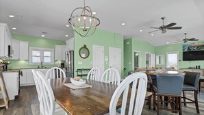 A spacious kitchen with white cabinets, a dining area with a wooden table and white chairs, and a ceiling fan. - New Management Beach, Elevator, Pool, Pet friendly (North Topsaile Beach)