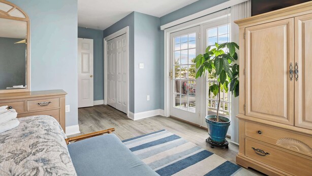 A bedroom with a bed, a dresser, a mirror, a potted plant, and a sliding glass door leading to a balcony. - Rooftop Tide | Ocean Views | Gas Fireplace (Salisbury)