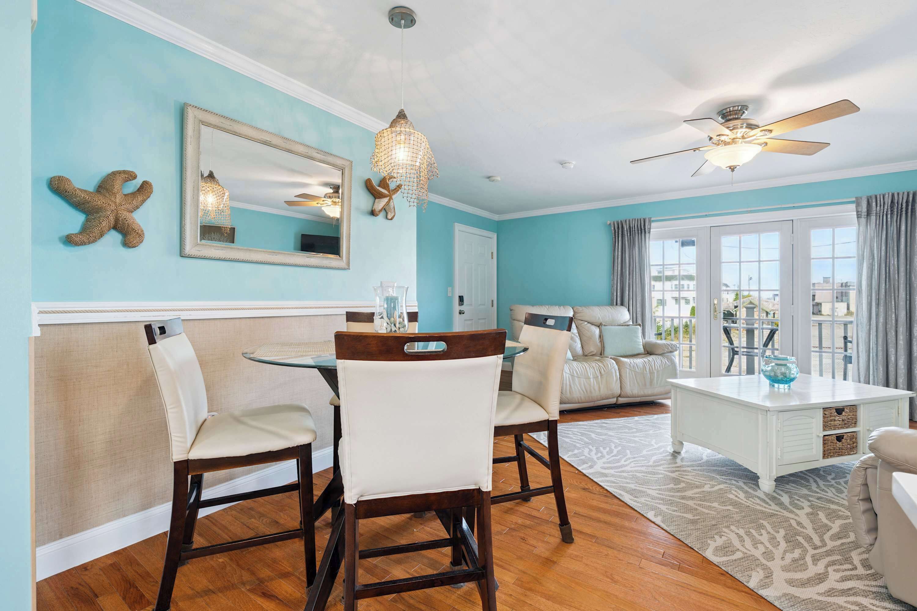 A dining area with a round table and chairs, a ceiling fan, and a large window with curtains.