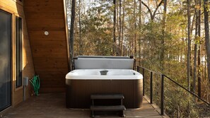 A wooden cabin with a hot tub on a deck, surrounded by trees.