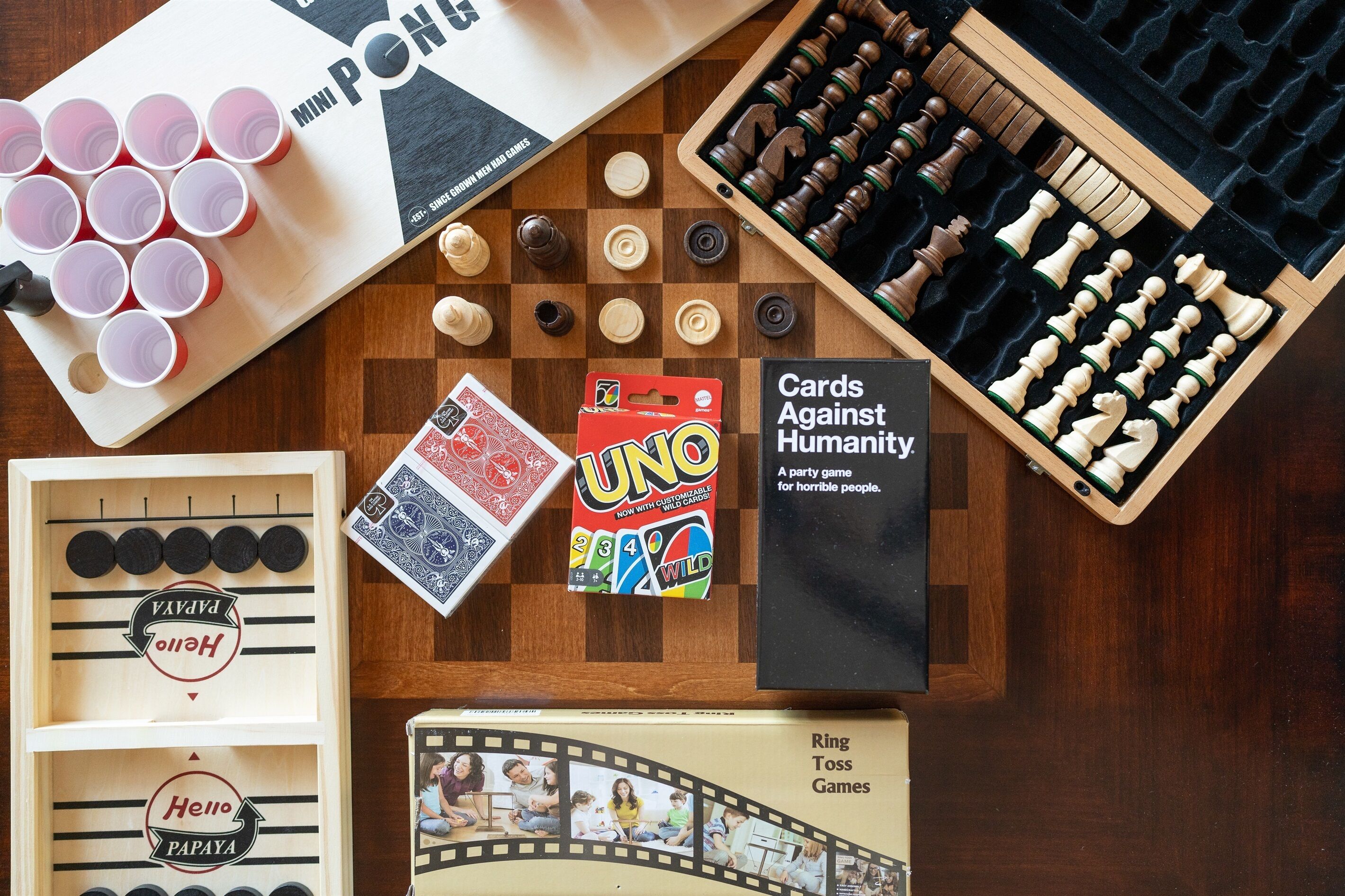 Een houten tafel met verschillende gezelschapsspellen en kaarten, waaronder UNO, Cards Against Humanity en Ring Toss Games.