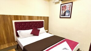 Ein ordentlich eingerichtetes Hotelzimmer mit einem Bett, einem Nachttisch, einer Wand-Klimaanlage und einem gerahmten Bild an der Wand.