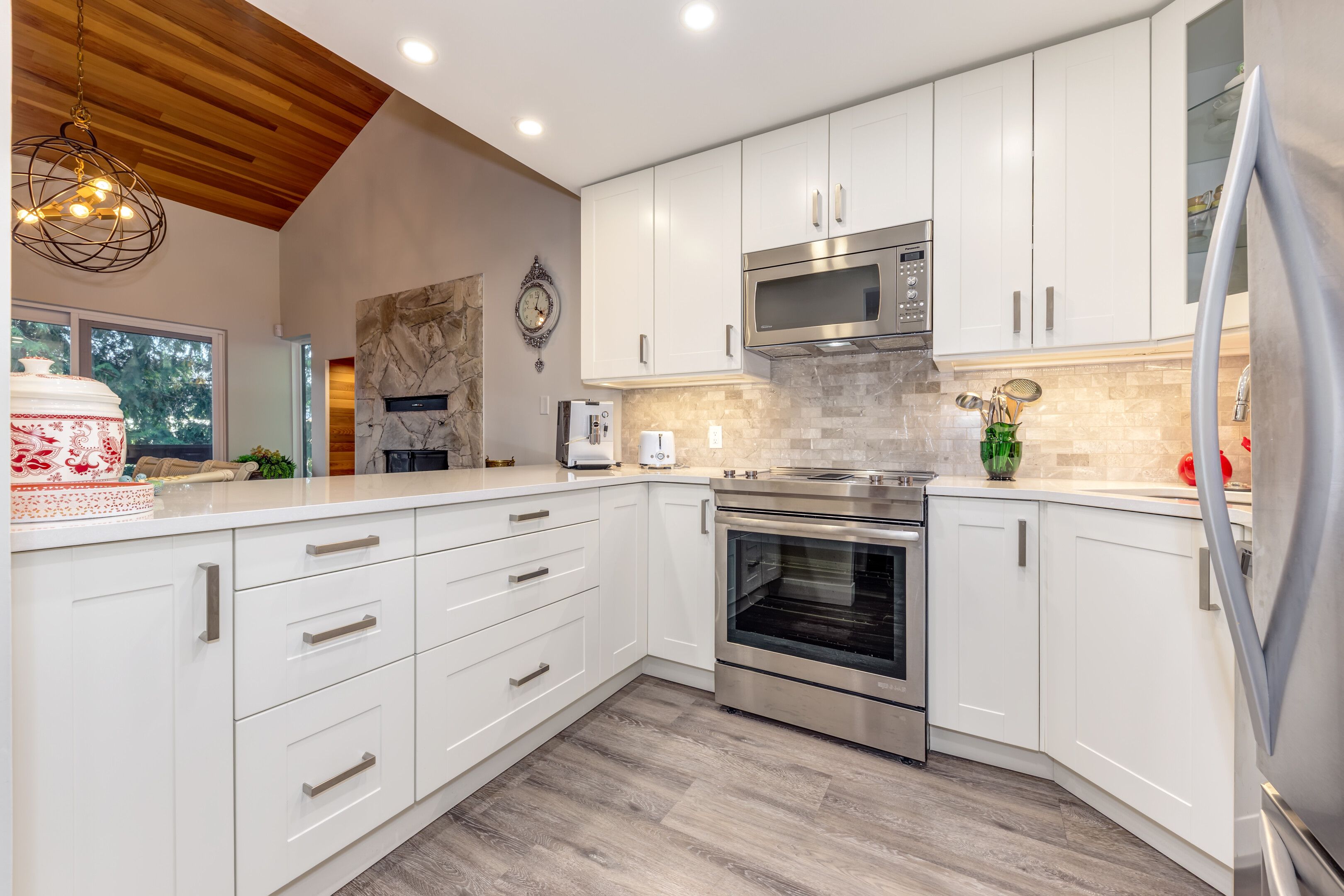 A modern kitchen with white cabinetry, stainless steel appliances, and a wooden ceiling.