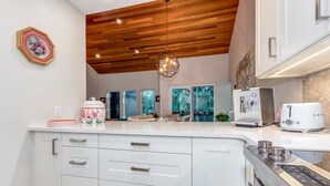 A modern kitchen with white cabinetry, a wooden ceiling, and a stone backsplash. - Telemark 18 - Ski in Walk out,  Short Walk to the Village, New Listing! (Whistler)