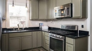 A kitchen with light green cabinets, a black countertop, a stainless steel stove, and a microwave. - Sweet & Petite Midtown Cottage for 5-Long Stays Welcome (Billings)