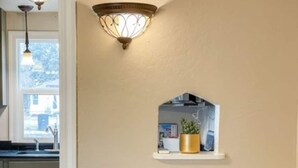 A kitchen with a countertop, a sink, and a window. There is a shelf with a plant and a decorative item. - Sweet & Petite Midtown Cottage for 5-Long Stays Welcome (Billings)