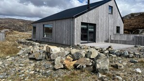 A modern wooden cabin with a sloped roof, large windows, and a stone foundation.