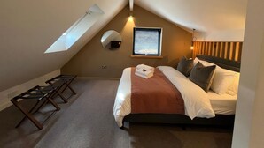 A bedroom with a sloped ceiling, a skylight, a bed with a white and brown bedspread, a bedside table, and a mirror.