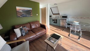 A modern living room with a brown leather sofa, a glass dining table, and a kitchen in the background. - 3 bedroom accommodation in Kylesku, near Lairg (Kylesku, near Lairg)