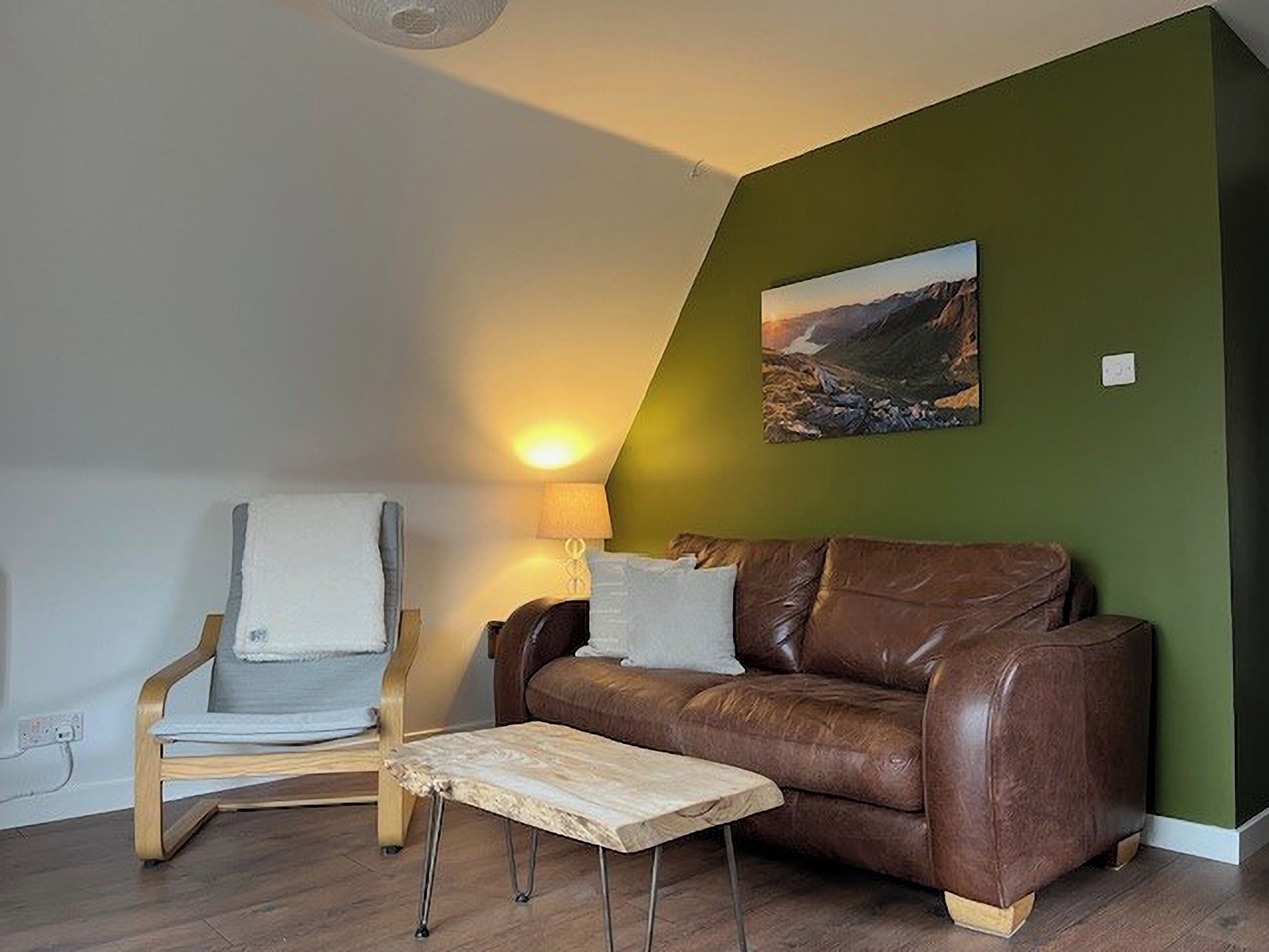 Ein Wohnzimmer mit einem braunen Ledersofa, einem Holzstuhl, einem kleinen Holztisch und einem Bild an der Wand.