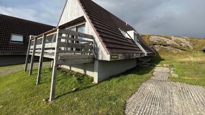 A modern house with a sloped roof and a wooden deck. - 3 bedroom accommodation in Kylesku, near Lairg (Kylesku, near Lairg)