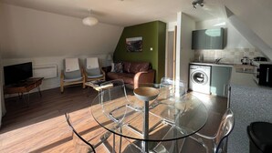 A compact living space with a dining area, a sofa, a TV, and a kitchen with a washing machine. - 3 bedroom accommodation in Kylesku, near Lairg (Kylesku, near Lairg)