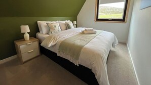 A bedroom with a bed, a nightstand, a lamp, a window with a view, and a green wall. - Steall Gorge - UK50495 (Kylesku, near Lairg)