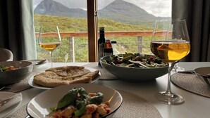 A dining table with a view of mountains, two glasses of wine, a bottle of Balsa Vines, and plates of food. - Steall Gorge - UK50495 (Kylesku, near Lairg)