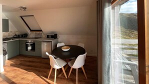 A modern kitchen with a dining area, featuring a black dining table, white chairs, and a view of the outdoors through a large window. - 3 bedroom accommodation in Kylesku, near Lairg (Kylesku, near Lairg)