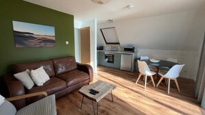 A cozy living room with a brown leather sofa, a wooden coffee table, and a dining area with white chairs and a black table. - 3 bedroom accommodation in Kylesku, near Lairg (Kylesku, near Lairg)