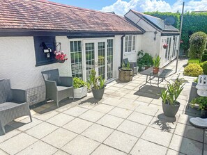 Een terras met rieten meubels, planten in potten, en een conservatorium met glazen deuren.