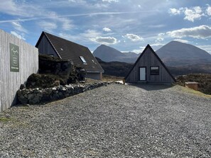 Un chalet en bois avec une allée en gravier, un mur en pierre et une vue sur les montagnes en arrière-plan.