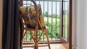 Uma cadeira de vime com almofada estampada numa varanda com guarda-corpo de metal, com vista para uma paisagem verde.