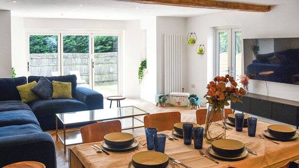 A modern living room with a sofa, dining table set for four, and a television mounted on the wall. - 4 bedroom accommodation in Little Dunham (Little Dunham)
